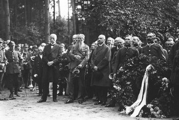 Grupa ludzi stojących w rzędzie, część z nich trzyma wieńce kwiatowe