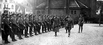 Mężczyźni w mundurach prezentują broń przed odbierającym defiladę